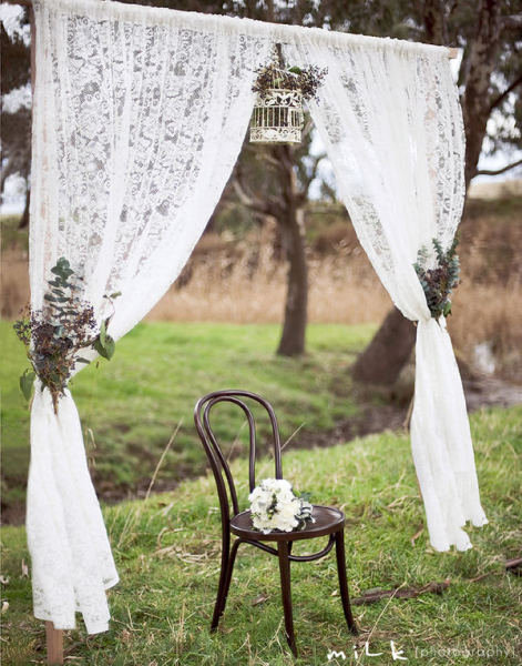 Dainty lace curtains, natural arrangements, and a delicate white birdcage create a rustic, elegant vibe.